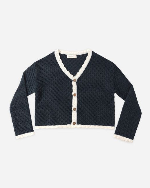 Navy blue cardigan with white trim and brown buttons on a light gray background