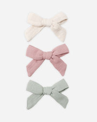 Three hair bows in cream, pink, and gray on a white background