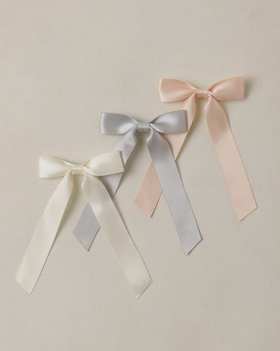 Three ribbon bows in white, gray, and pink on a beige background