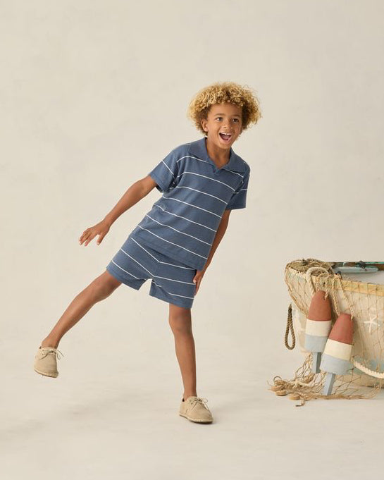 Child wearing a blue striped dress standing next to a woven basket on a beige background