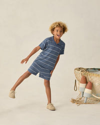 Child wearing a blue striped dress standing next to a woven basket on a beige background